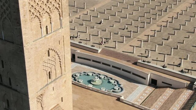 Detailed HD shot featuring the intricate Almohad-style stone carvings of the Hassan Tower in Rabat. The frame captures a beautiful geometric fountain and the vast square of ancient pillars in the back