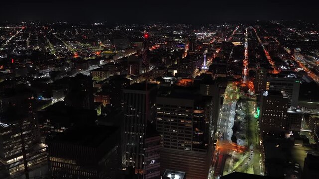 Night aerial over downtown Baltimore with illuminated skyline, busy streets and an American flag atop the William Donald Schaefer Building. Top down flyover. Peaceful nightscape scene in USA.