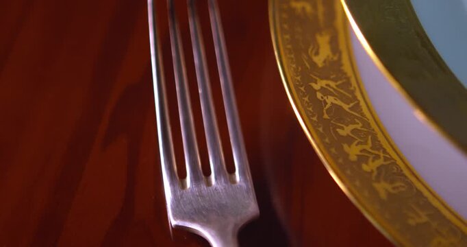 Detailed tracking shot reveals silverware and gold plated bowl on luxury dining table. Suitable for premium restaurant branding and elegant event themes.
