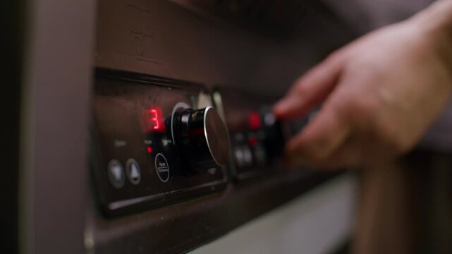 Hand of male chef adjusting temperature control dial on modern oven with digital display while preparing for baking food in restaurant kitchen. Close up view