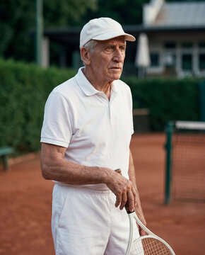 Focused Senior Tennis Player in White Cap on a Clay Court