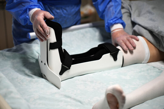 Medical Professional Adjusting Ankle Orthosis Brace. Doctor carefully correcting the fit of a orthopedic ankle foot orthosis (AFO) for a patient in a hospital bed. Focused on clinical rehabilitation