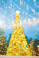 Large festive Christmas tree bright golden lights colorful ornaments and a star topper outdoor night