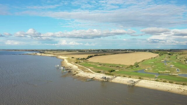 Aerial view of a scenic coastline with sandy beaches, fishing huts on stilts, open fields, and blue sky near La Rochelle, France.