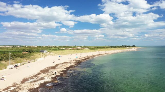 Aerial view of a sandy beach with turquoise water and scattered visitors on ile de Re, France, under a blue sky with clouds.