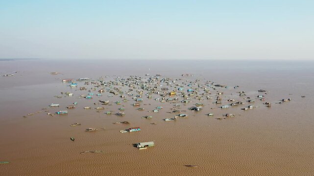 Aerial view of the floating village of Chong Kneas on Tonle Sap Lake, Cambodia, with numerous houses and boats scattered across the water under a clear sky.