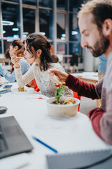 A group of business employees enjoy a meal at a bright office cafeteria, sharing food and...