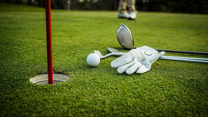 Golf Ball and Clubs Near Hole with Red Flag on Green Turf