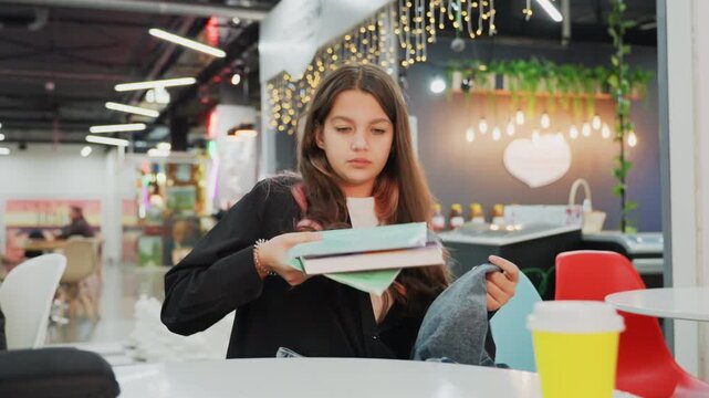 young student studying at mall cafe, soft string lights, cozy table with notebook and pink pencil case, yellow takeaway cup, denim sweater draped over lap, hands sorting notes while preparing