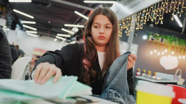 young student studying at cafe table, sorting notebooks, folding sweater, flipping textbook pages by yellow cup, warm string lights and soft bokeh, focused and contemplative preparing for exam