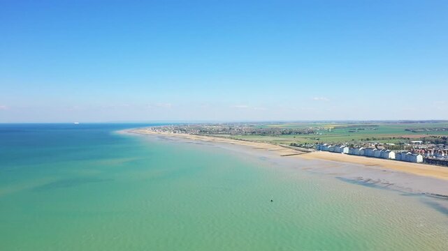 Wide aerial shot of Juno Beach and the coastline at Bernieres sur Mer, Normandy, France, featuring turquoise water, sandy shore, and coastal village under a clear blue sky.