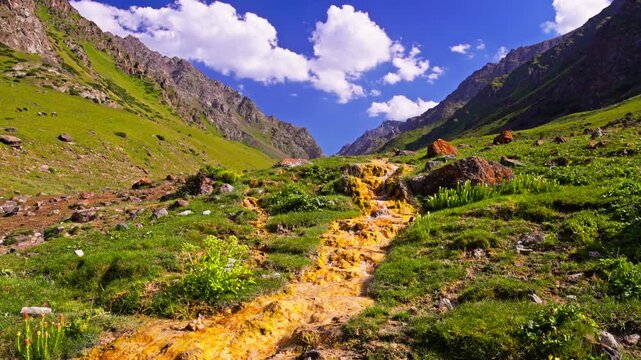 Mountain landscape with iron-oxidizing bacteria creek and summer greenery under a blue sky with white clouds in Kyrgyzstan.