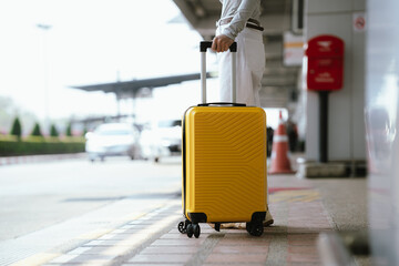 Close-up of traveler pulling yellow suitcase at airport curbside, ready for departure and transportation. © Witoon