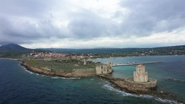 Drone shot of historic Methoni Castle on the coast with dramatic clouds and turquoise waters, located in Methoni, Greece.