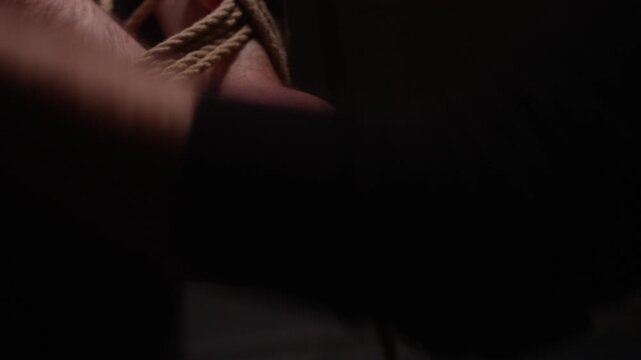 Close-up of hands tied with rope in dim light, creating tension