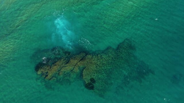Drone shot of clear turquoise water with a rocky reef and gentle waves near Acciaroli, Italy. Natural coastal scenery ideal for travel and nature concepts.