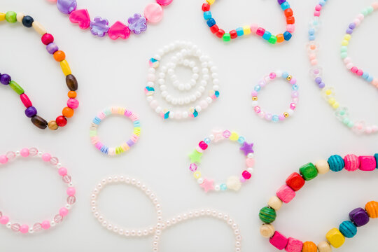 Bracelets and necklaces for little child girl on light gray table background. Created beaded jewellery from colorful different plastic parts. Closeup. Flat lay. Top down view.
