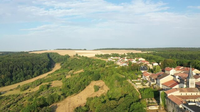 Scenic aerial shot of Hattonchatel village surrounded by lush green forests, rolling hills, and farmland under a blue sky.