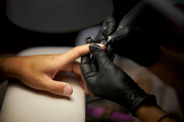 Fototapeta premium Men's manicure. Male hand undergoing a manicure procedure. The master does a man's manicure. A manicurist files a man's nails in a salon. Hygiene and hand care for men. Men's manicure design.