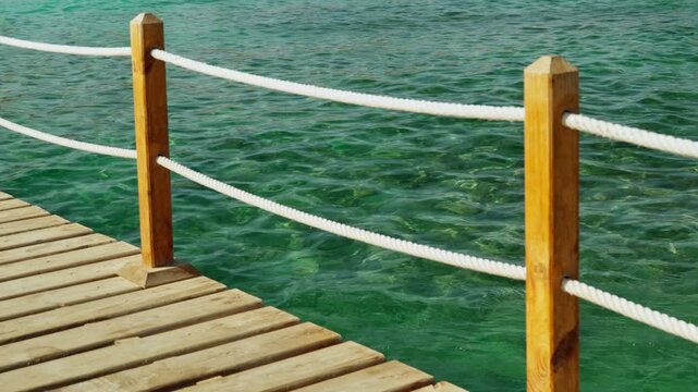 The protective rope fence of the pier for boat trips overlooking the calm turquoise waters.