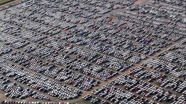 Aerial drone view of thousands of new cars parked in symmetrical rows at the massive vehicle import and export storage terminal in Grimsby, UK.