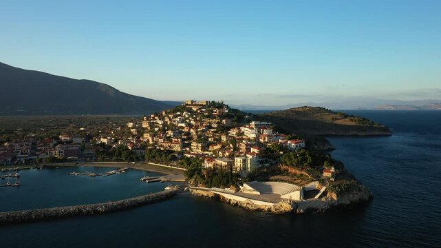 Scenic aerial view of Paralio Astros, a picturesque coastal town in Greece, featuring traditional houses, a harbor, and dramatic coastline at sunset.