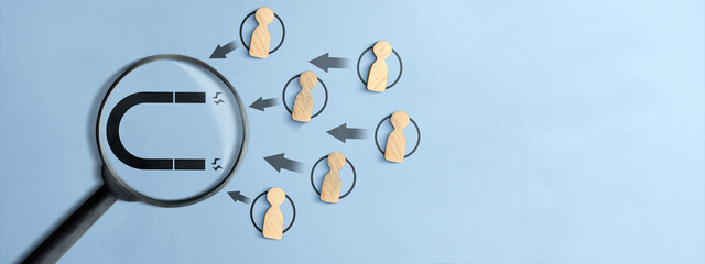Top view of wooden figures being drawn by a magnet icon through a magnifying glass on a light blue background. Illustrates lead generation, HR recruitment, and client acquisition concepts