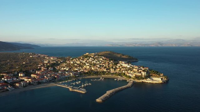 Scenic aerial shot of Paralio Astros, a picturesque coastal town in Greece with a marina, traditional buildings, and clear blue sea under a bright sky.