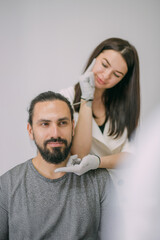 Fototapeta premium Portrait of a young beautiful woman beautician in a medical white uniform and a young bearded man patient