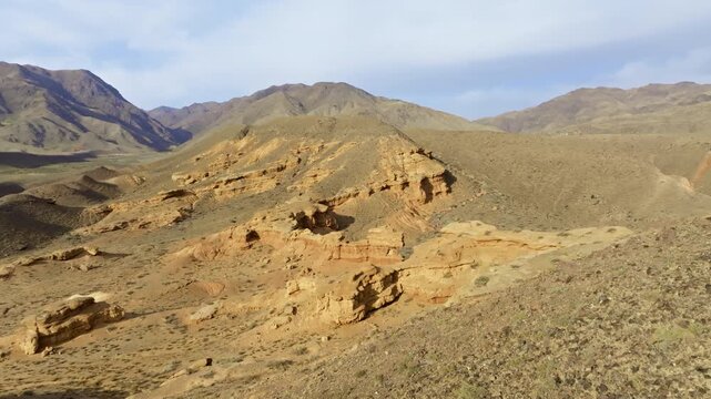 Expansive aerial view captures majestic rock formations in Kyrgyzstan. Serene landscape showcases arid terrain, mountains, and eroded sandstone yardang canyons.