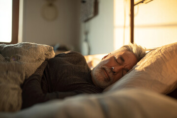 senior man sleeping peacefully on side in bed, soft morning sunlight, warm and cozy bedroom.
