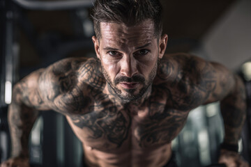 Obraz premium athletic tattooed man training in modern gym, detailed ink on arms and chest, focused expression, bright indoor lighting, dynamic composition.
