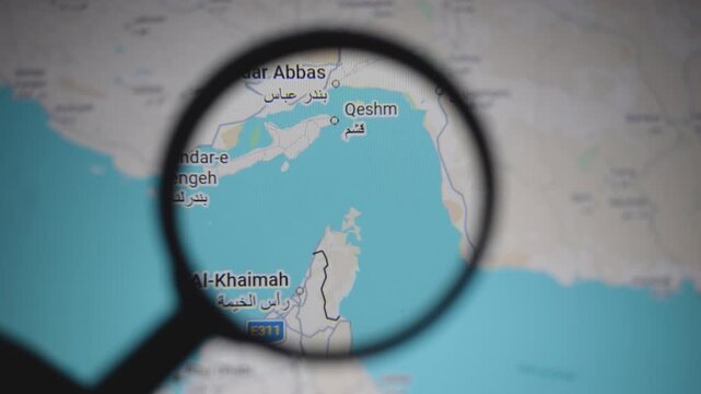 Close up of map showing Strait of Hormuz and Persian Gulf region under magnifying glass, highlighting geopolitical tensions, oil supply routes, and strategic location between Iran, Oman and UAE waters