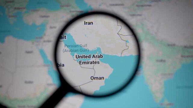 Close up of map showing Strait of Hormuz and Persian Gulf region under magnifying glass, highlighting geopolitical tensions, oil supply routes, and strategic location between Iran, Oman and UAE waters