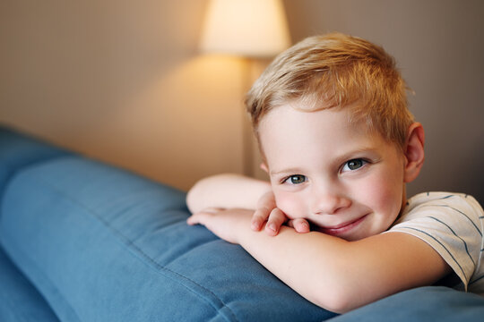 A beautiful close-up portrait of a happy little boy leaning on a sofa and smiling. Image captures pure childhood joy and innocence. Perfect for kids healthcare and education advertising.