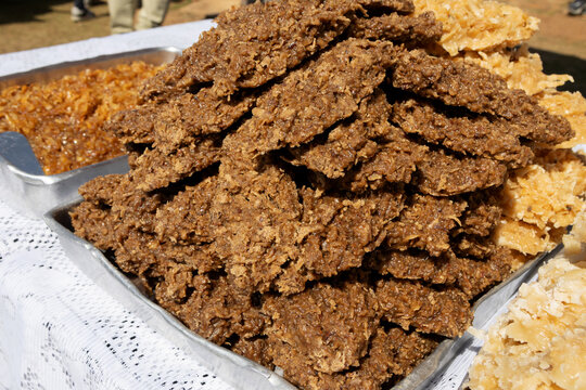 High-angle close-up of dark brown Brazilian cocada coconut candies. Bright natural light highlights their textured, rustic surface.