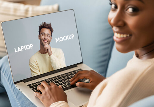 Closeup template of colored woman using laptop at home  in living room on sofa, looking at camera