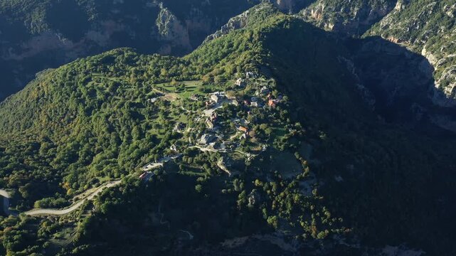 Drone shot of a traditional mountain village surrounded by lush green hills and dramatic cliffs in Vikos, Greece. Picturesque rural landscape with winding roads and dense forest.
