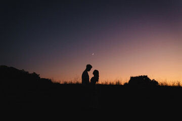 Fototapeta premium Silhouette of romantic couple at sunset under crescent moon