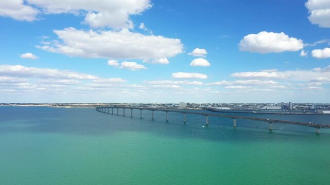 A long bridge stretches across turquoise waters under a bright blue sky with scattered clouds, connecting the mainland to ile de Re, France.