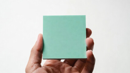Fototapeta premium Hand holding a blank green sticky note against a white background for notes and reminders