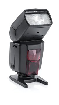 Angled studio-style camera flash unit, black body with a red accent, illuminating lens, on a white background