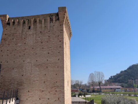 Torre medievale in mattoni chiari svetta in un paesaggio collinare dell&rsquo;Italia centrale, caratterizzata da merlature e piccole aperture che richiamano l&rsquo;architettura difensiva storica