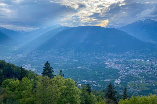 Panoramic view over Merano and Burgraviato in Adige Valley; Vinschgau (Val Venosta) and Oetztal Alps beyond, Ultental (Val d'Ultimo) to the left under sunbeams and a cloudy sky in South Tyrol, Italy