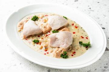 Poached chicken in a creamy white bean sauce on a white plate, garnished with fresh herbs and red pepper flakes. Plated for a professional menu or food blog