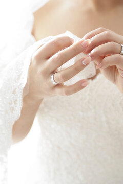 Bride's hands with wedding ring and delicate lace detail on her dress
