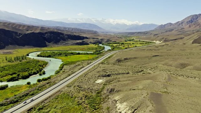 Cars travel along a scenic highway surrounded by majestic mountain landscape of Boom gorge and a flowing Chu river. Drone view with dolly forward camera movement.