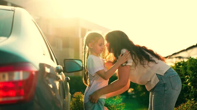 Happy Mother hugs little girl getting ready for primary school lesson in schoolyard. Mom walks daughter school with backpack, hugging on street next to car. Family happiness. Childs education. Kid mom