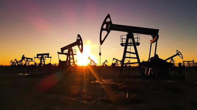 Silhouettes of numerous oil pumpjacks working in a vast field during a vibrant sunset