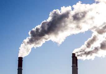 CHP emissions. Smoking chimney releasing smoke against a blue sky. Smoke from factory pipe of heat...
